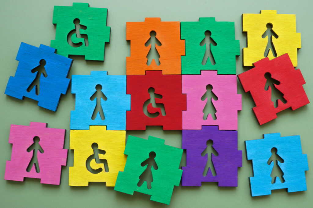Bunte Puzzleteile mit Symbolen von Menschen und Rollstuhlfahrern auf grünem Hintergrund.